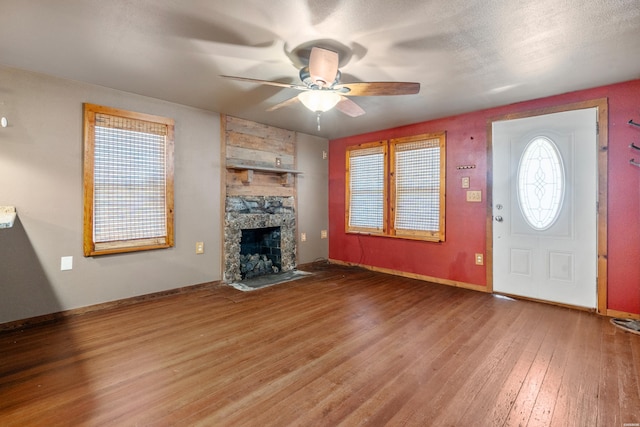 unfurnished living room featuring ceiling fan, a fireplace, wood finished floors, and baseboards