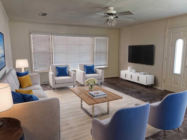 living room featuring a textured ceiling, wood finished floors, visible vents, a ceiling fan, and ornamental molding