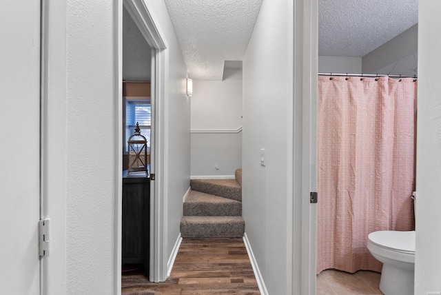 bathroom with toilet, a textured ceiling, baseboards, and wood finished floors