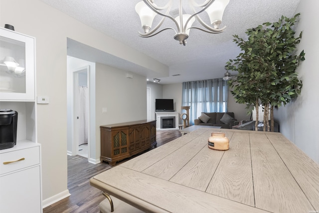 interior space featuring a textured ceiling, a notable chandelier, a fireplace, baseboards, and dark wood finished floors