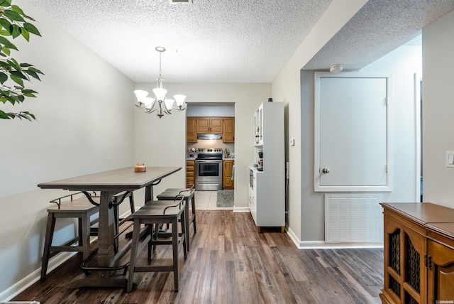 dining space with dark wood finished floors, visible vents, an inviting chandelier, a textured ceiling, and baseboards