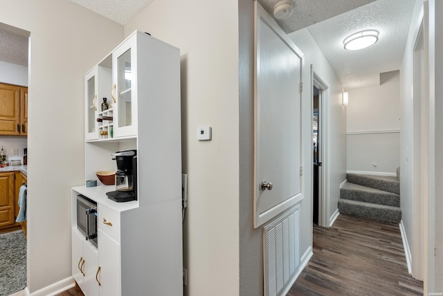 hall featuring a textured ceiling, dark wood-type flooring, visible vents, and baseboards