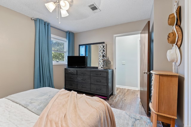 bedroom featuring light wood finished floors, visible vents, baseboards, a ceiling fan, and a textured ceiling