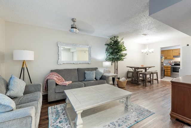 living area featuring an inviting chandelier, a textured ceiling, visible vents, and wood finished floors