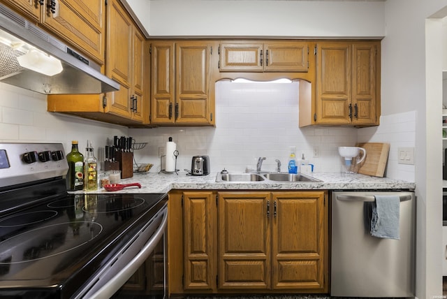 kitchen with tasteful backsplash, appliances with stainless steel finishes, brown cabinets, under cabinet range hood, and a sink