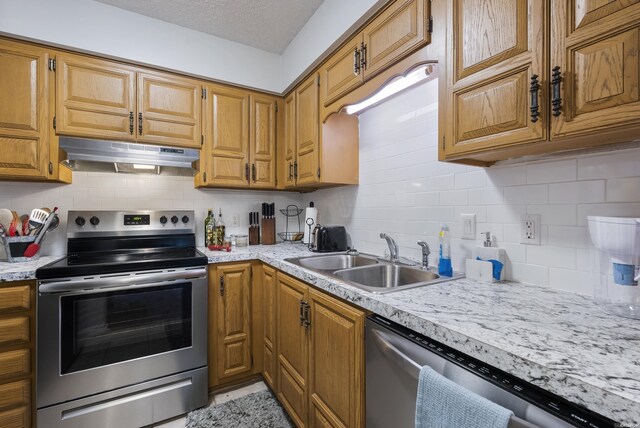 kitchen featuring stainless steel appliances, brown cabinetry, a sink, a textured ceiling, and under cabinet range hood