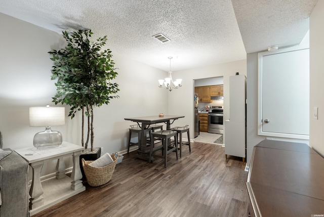 dining space with a notable chandelier, visible vents, a textured ceiling, wood finished floors, and baseboards