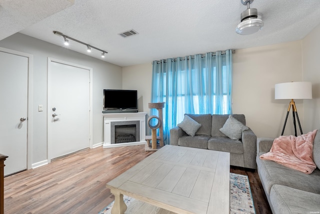 living area featuring a textured ceiling, a fireplace, wood finished floors, and visible vents