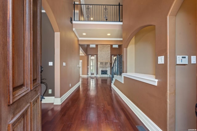 foyer entrance featuring visible vents, baseboards, a fireplace, a towering ceiling, and dark wood-style flooring