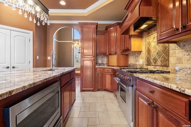 kitchen featuring ornamental molding, a sink, arched walkways, appliances with stainless steel finishes, and custom exhaust hood