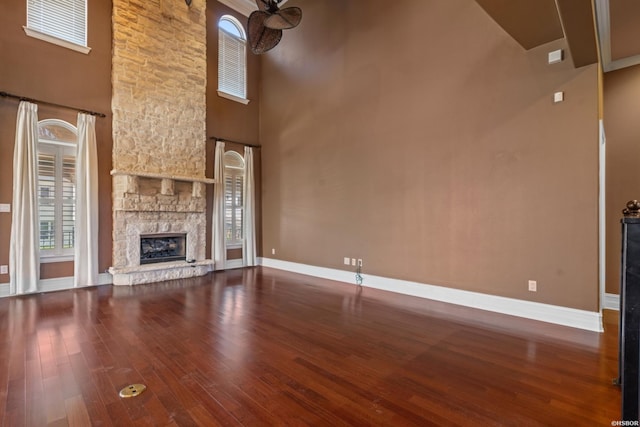 unfurnished living room featuring wood finished floors, a fireplace, baseboards, and a towering ceiling