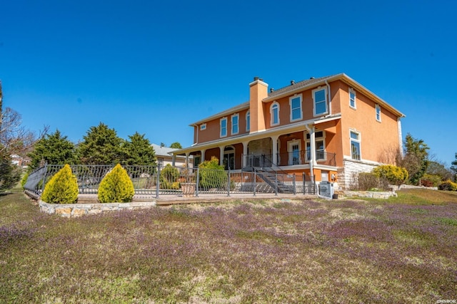 back of property with stucco siding, a porch, fence, and a chimney