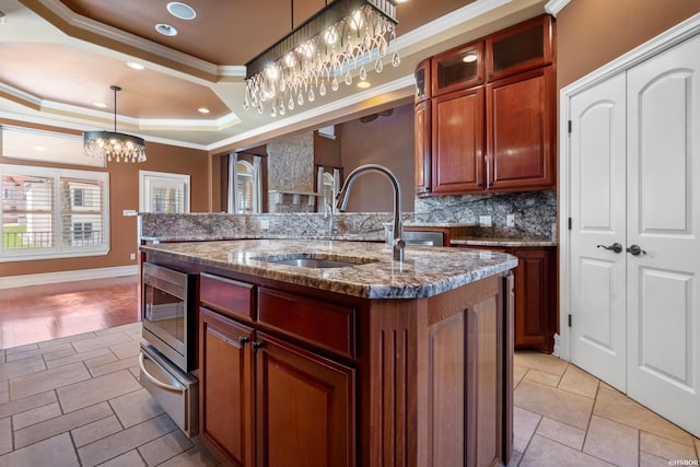 kitchen featuring an island with sink, ornamental molding, a raised ceiling, a warming drawer, and a sink