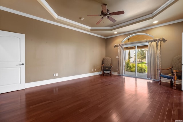 unfurnished room featuring a raised ceiling, wood finished floors, baseboards, and ornamental molding