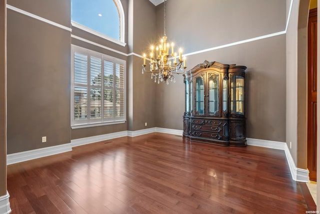 interior space featuring baseboards, a high ceiling, an inviting chandelier, and wood finished floors