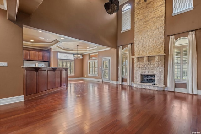 unfurnished living room featuring a healthy amount of sunlight, a stone fireplace, wood finished floors, and ornamental molding