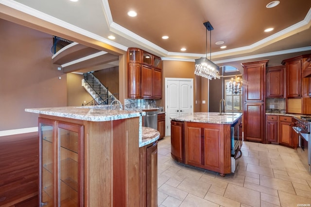 kitchen with an island with sink, a sink, glass insert cabinets, a raised ceiling, and light stone countertops