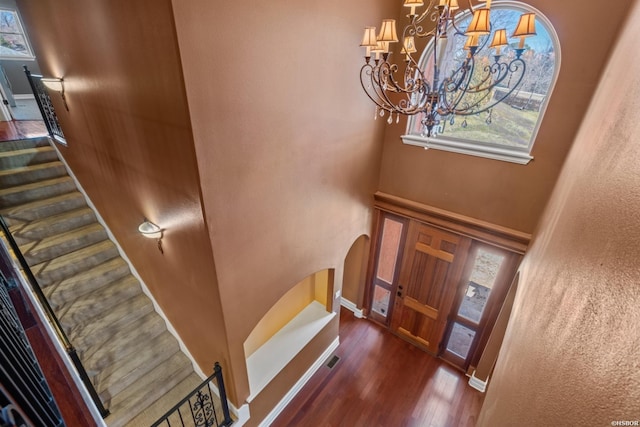 foyer entrance with wood finished floors, arched walkways, an inviting chandelier, baseboards, and stairs