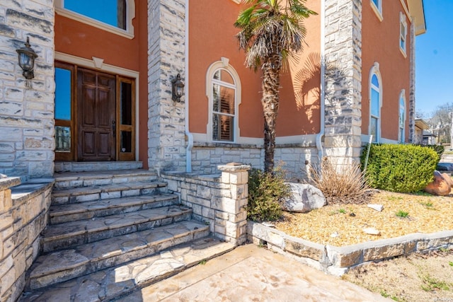 view of exterior entry featuring stucco siding and stone siding