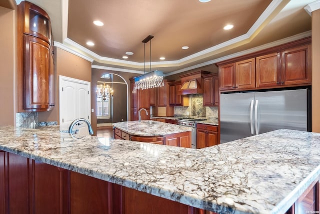 kitchen with premium range hood, an island with sink, a tray ceiling, a peninsula, and stainless steel appliances