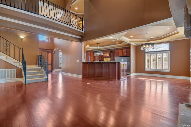 unfurnished living room featuring visible vents, stairway, ornamental molding, arched walkways, and a raised ceiling