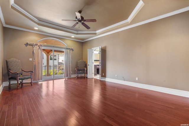 interior space featuring a ceiling fan, wood finished floors, baseboards, a tray ceiling, and crown molding