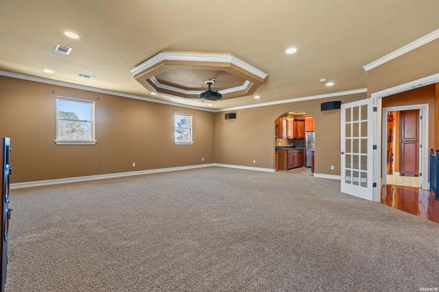 carpeted spare room featuring visible vents, baseboards, a tray ceiling, arched walkways, and a ceiling fan