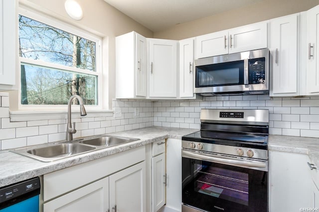 kitchen with tasteful backsplash, appliances with stainless steel finishes, light countertops, white cabinetry, and a sink