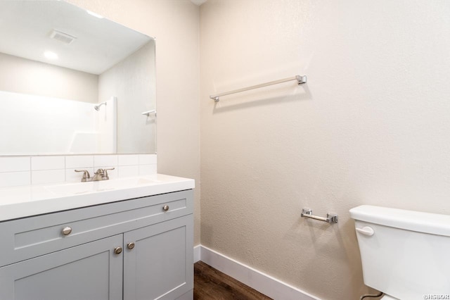 bathroom featuring toilet, wood finished floors, vanity, visible vents, and tasteful backsplash