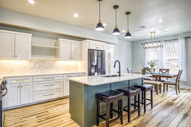 kitchen with a kitchen island with sink, a sink, white cabinetry, light countertops, and stainless steel refrigerator with ice dispenser