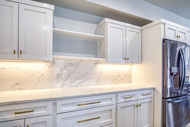 kitchen featuring white cabinets, light stone counters, stainless steel refrigerator with ice dispenser, open shelves, and backsplash