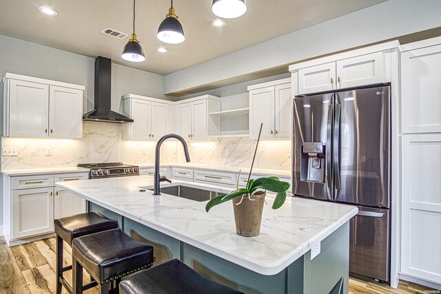 kitchen featuring a kitchen island with sink, wall chimney exhaust hood, white cabinets, and stainless steel appliances