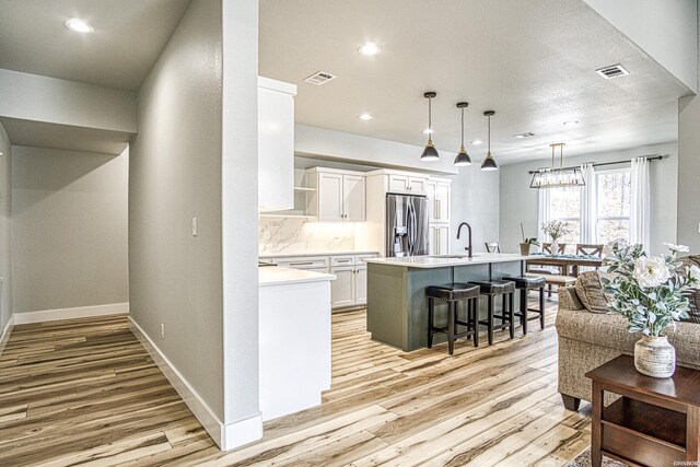 kitchen featuring light countertops, visible vents, a kitchen island with sink, white cabinets, and stainless steel fridge with ice dispenser