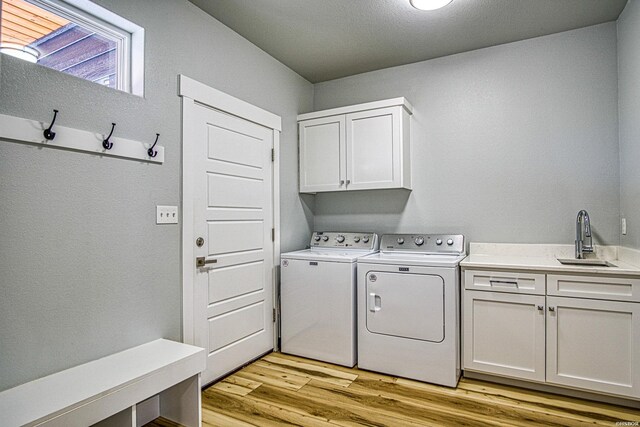 washroom with light wood-type flooring, cabinet space, a sink, and washing machine and clothes dryer