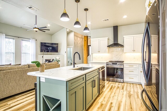 kitchen featuring black refrigerator, a sink, stainless steel range oven, wall chimney exhaust hood, and an island with sink