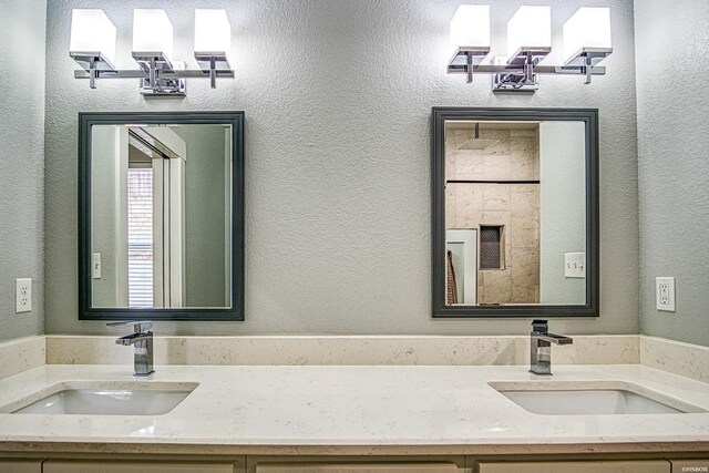 full bath with a textured wall, double vanity, and a sink