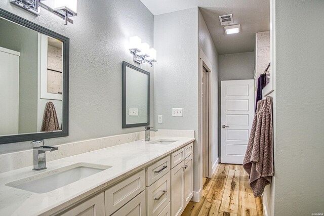 bathroom with double vanity, visible vents, a sink, and wood finished floors