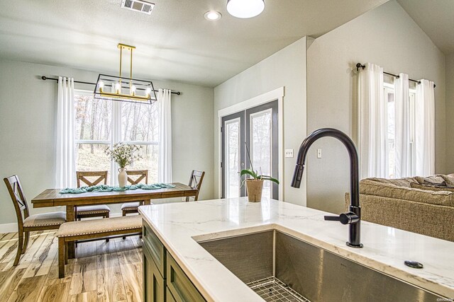 kitchen with light stone counters, pendant lighting, visible vents, a sink, and light wood-type flooring