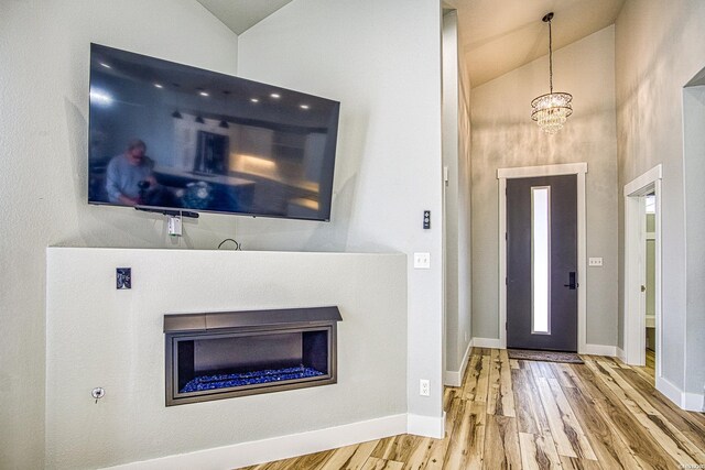 foyer with lofted ceiling, a notable chandelier, baseboards, and wood finished floors