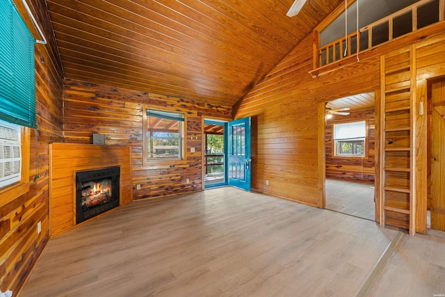 unfurnished living room with plenty of natural light, a lit fireplace, wood walls, and wooden ceiling