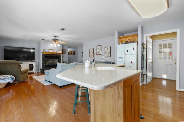 kitchen featuring a breakfast bar area, open floor plan, a kitchen island with sink, a sink, and white fridge with ice dispenser