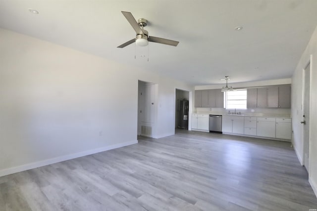 unfurnished living room featuring light wood finished floors, visible vents, a sink, baseboards, and ceiling fan with notable chandelier