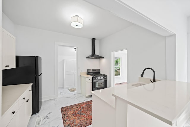 kitchen with stainless steel range with gas stovetop, a sink, freestanding refrigerator, marble finish floor, and wall chimney exhaust hood