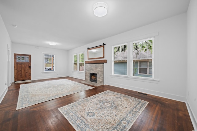 living area with baseboards, visible vents, a stone fireplace, and wood finished floors