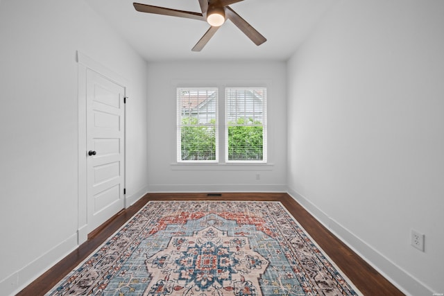 empty room featuring dark wood-type flooring, a ceiling fan, and baseboards