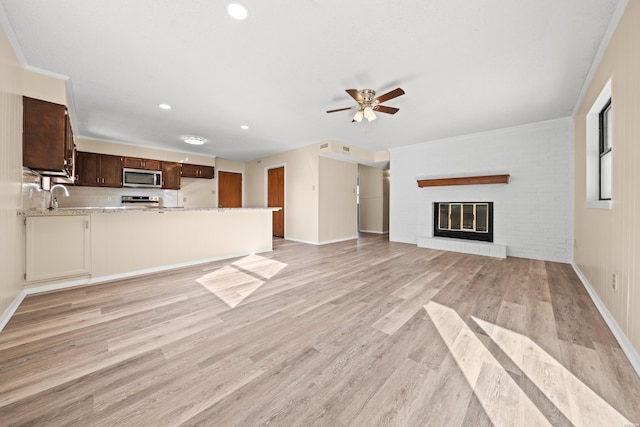 unfurnished living room featuring ornamental molding, light wood-type flooring, a fireplace, and a sink