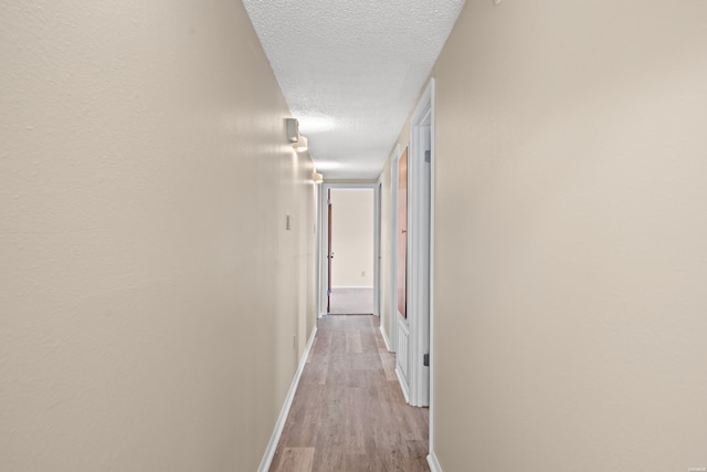 hallway featuring a textured ceiling, light wood-style flooring, and baseboards