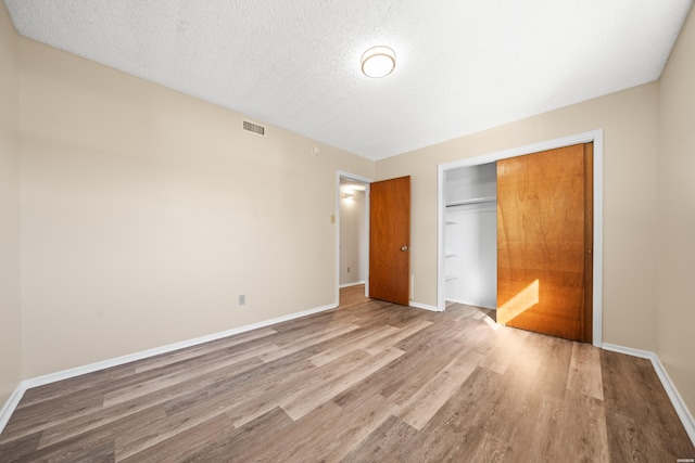 unfurnished bedroom featuring a closet, visible vents, baseboards, and wood finished floors