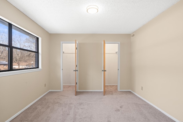 unfurnished bedroom with baseboards, light colored carpet, a walk in closet, a textured ceiling, and a closet