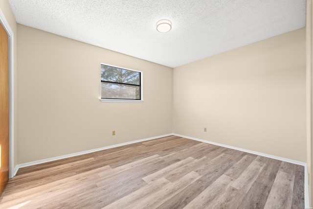 spare room featuring light wood-style floors, baseboards, and a textured ceiling